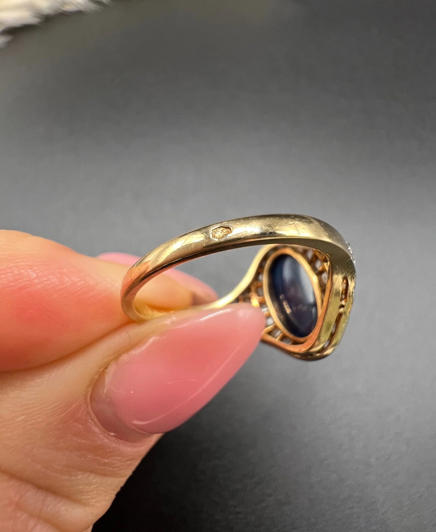 An oval cabochon sapphire and diamond fancy cluster ring in yellow and white gold, held in a hand