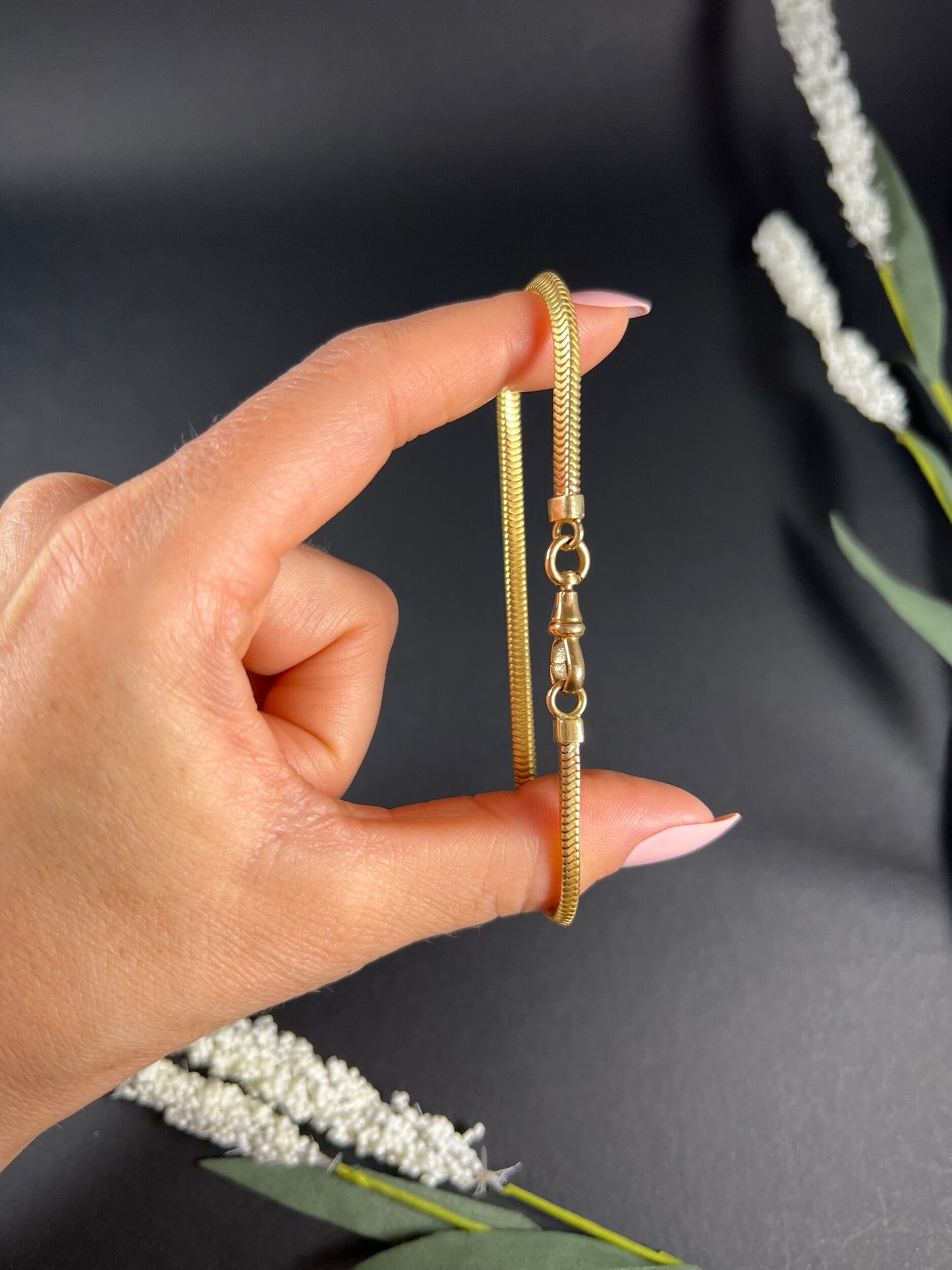 A yellow gold snake link bracelet, held in a hand