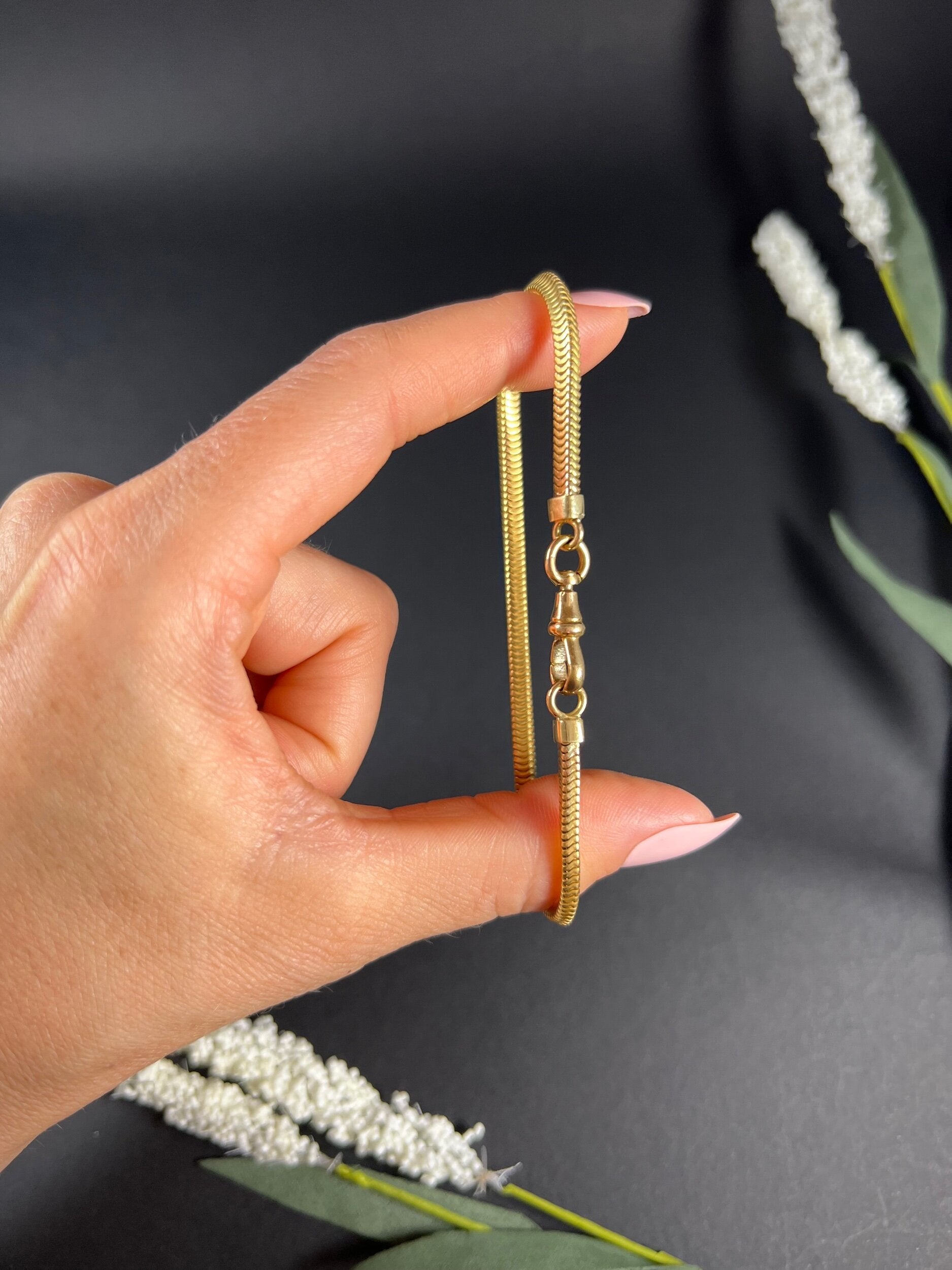 A yellow gold snake link bracelet, held in a hand
