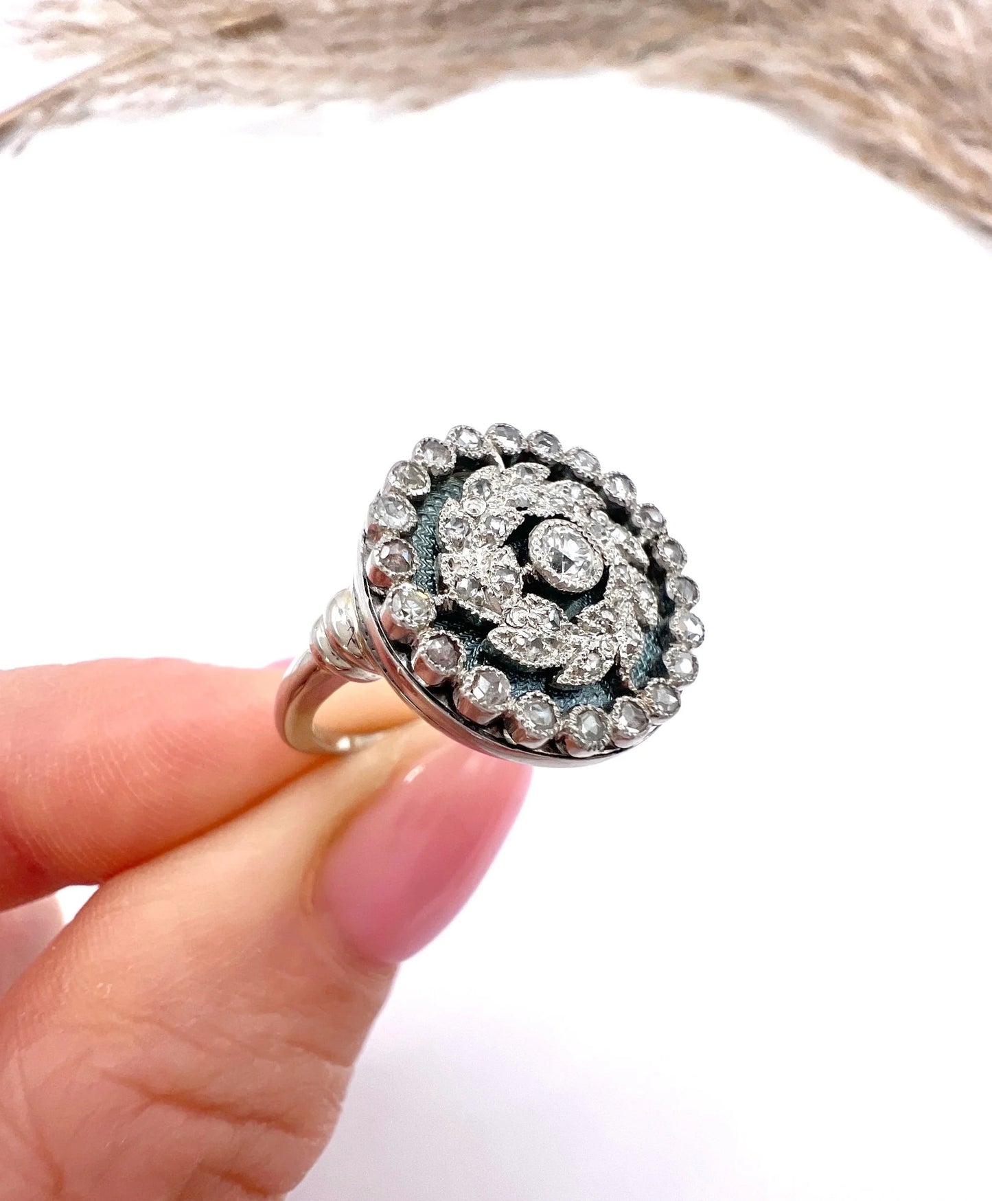 A diamond and dark blue enamel fancy cluster ring in white gold, held in a hand