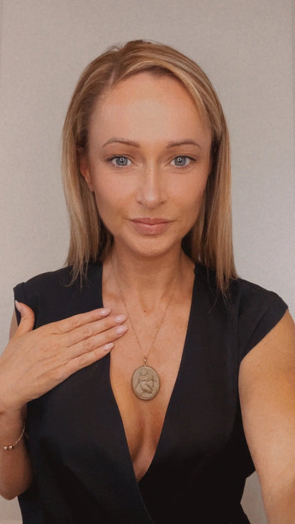 An oval cherub lava cameo pendant in yellow gold, with a chain, modelled by a woman