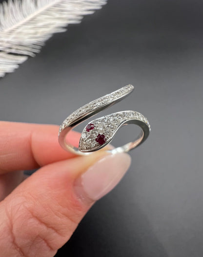 A white gold snake ring set with diamonds and with ruby eyes, held in a hand