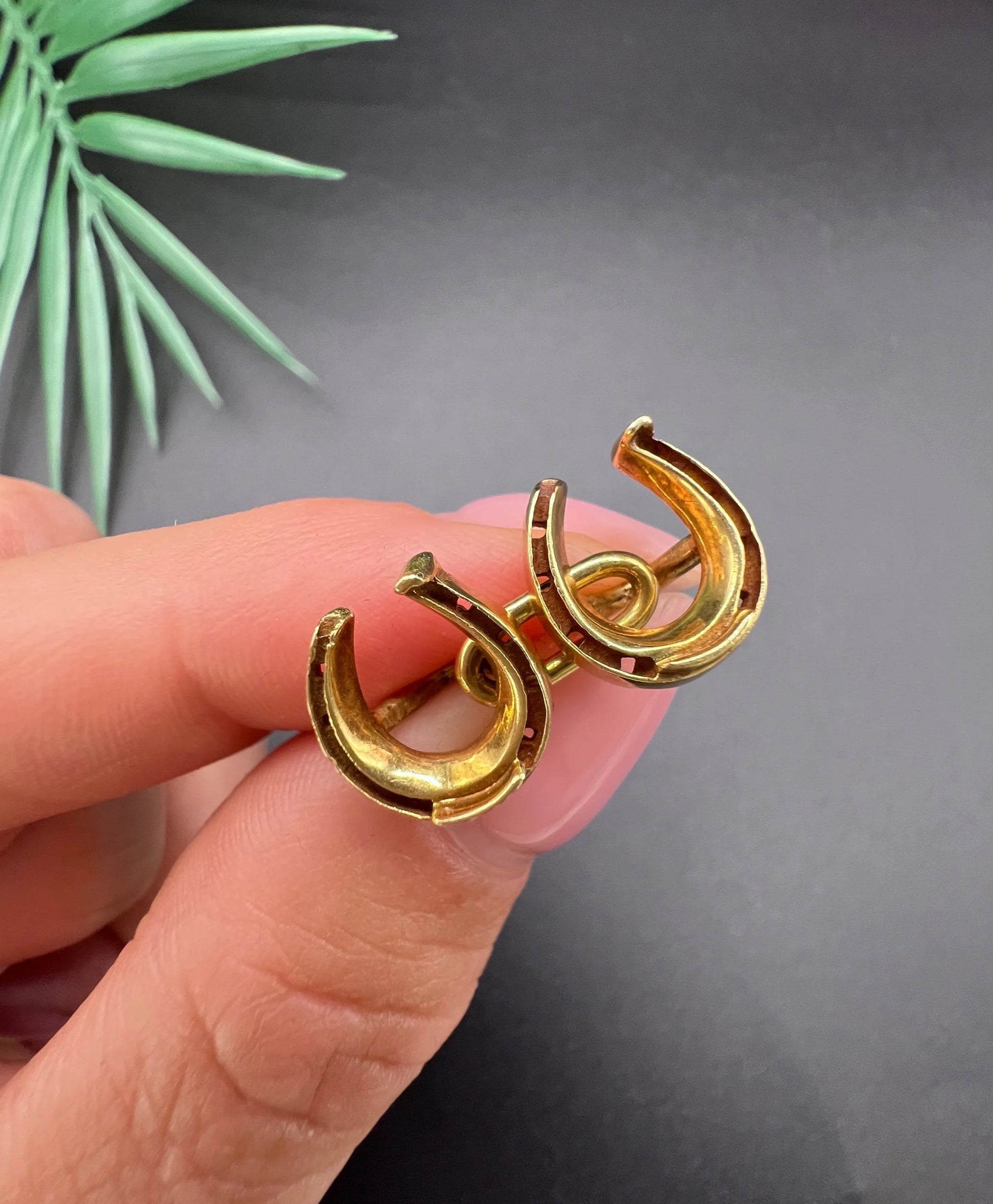 A pair of double-sided horseshoe cufflinks in yellow gold, held in a hand