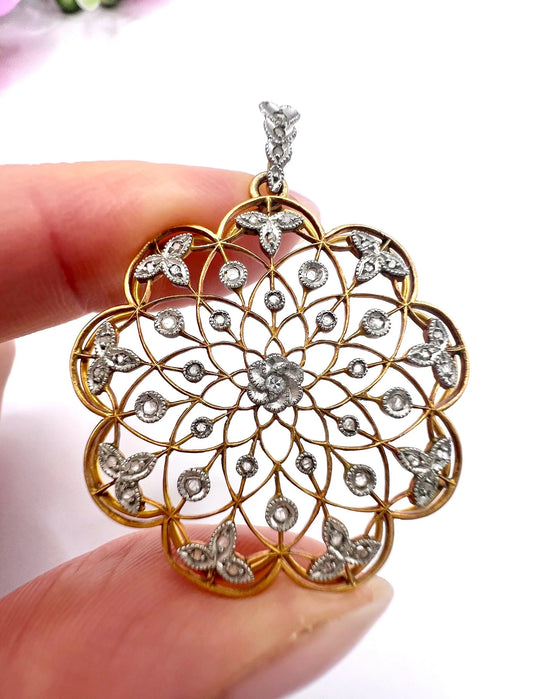A floral openwork diamond pendant in gold and platinum, held in a hand