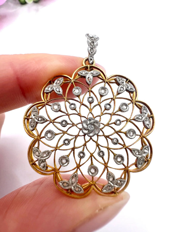 A floral openwork diamond pendant in gold and platinum, held in a hand