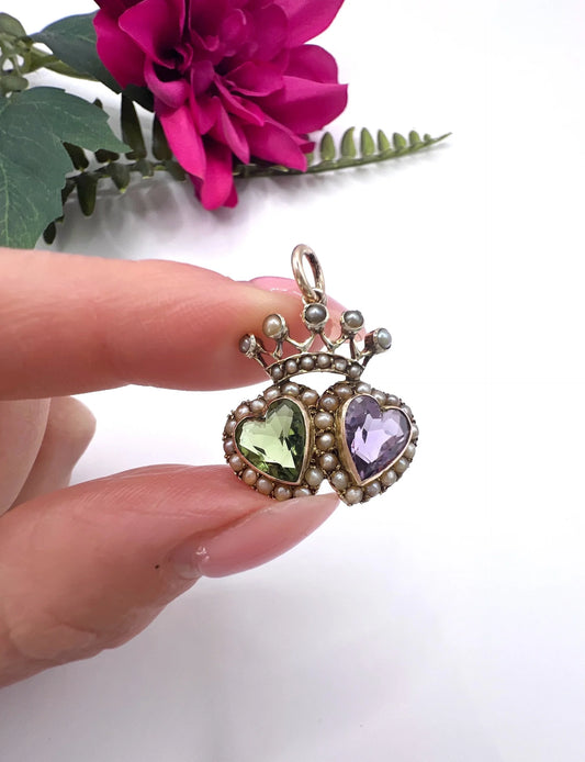 A double heart and crown pendant with peridot, amethyst and pearls in yellow gold, held in a hand