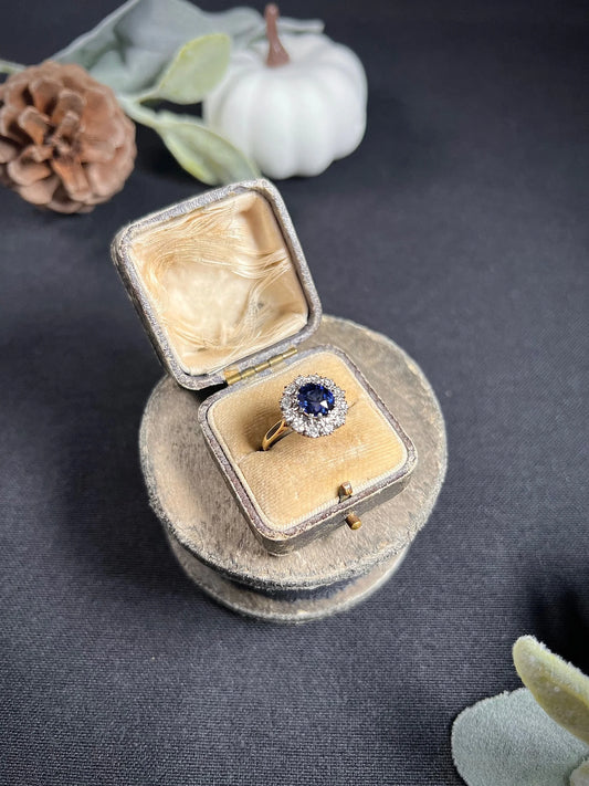 A round sapphire and diamond cluster ring, in an antique ring box