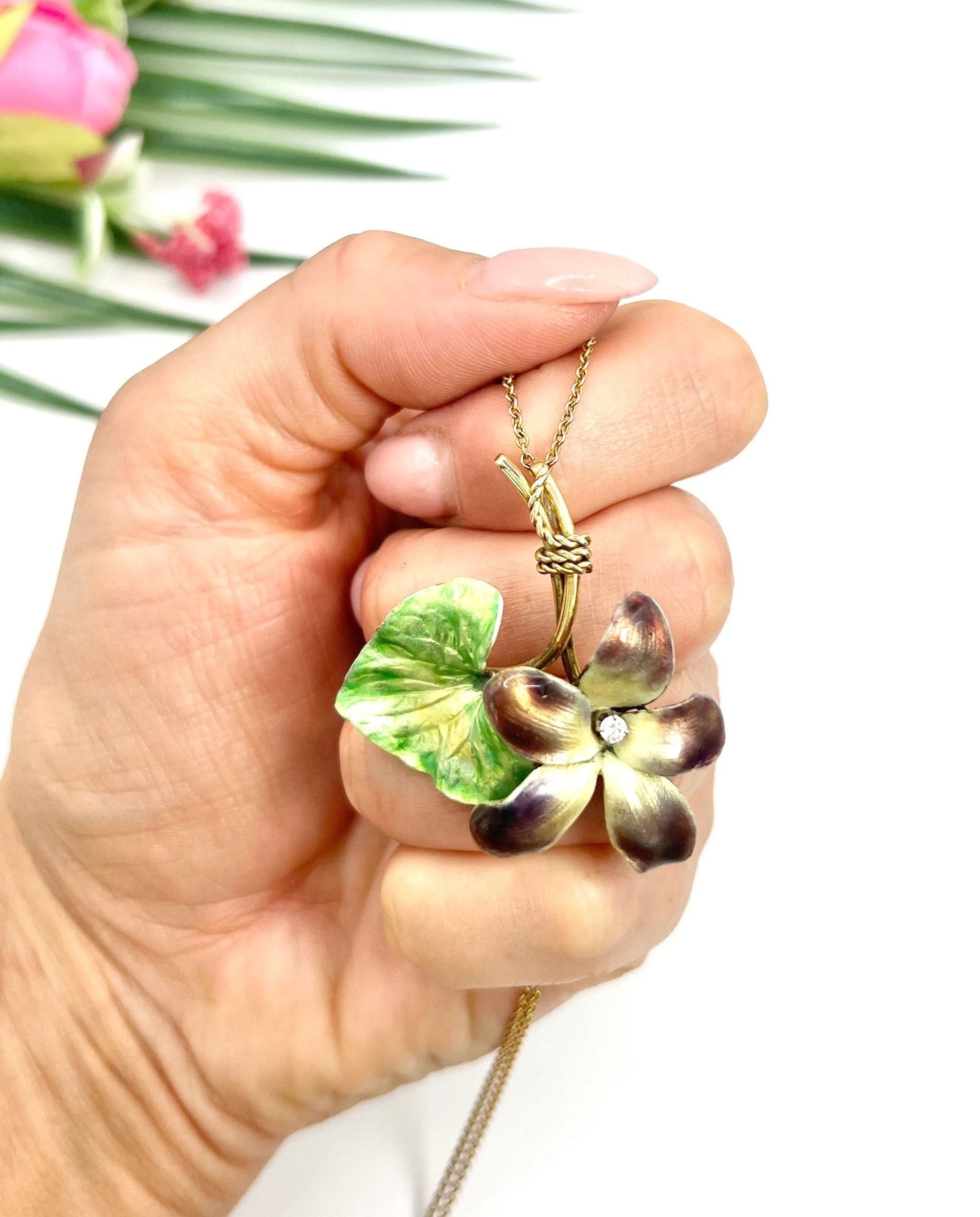 Gold and enamel diamond flower pendant with a gold chain, held in a hand