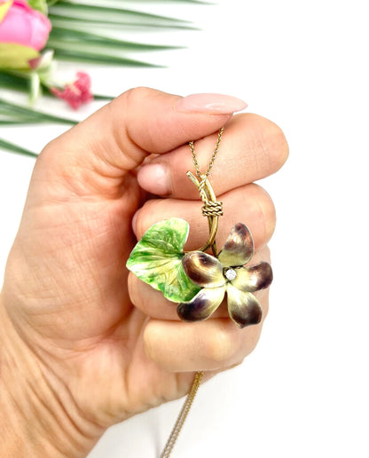 Gold and enamel diamond flower pendant with a gold chain, held in a hand