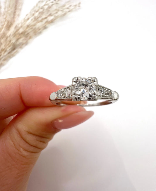 A solitaire diamond ring in platinum, with diamond set shoulders, held in a hand
