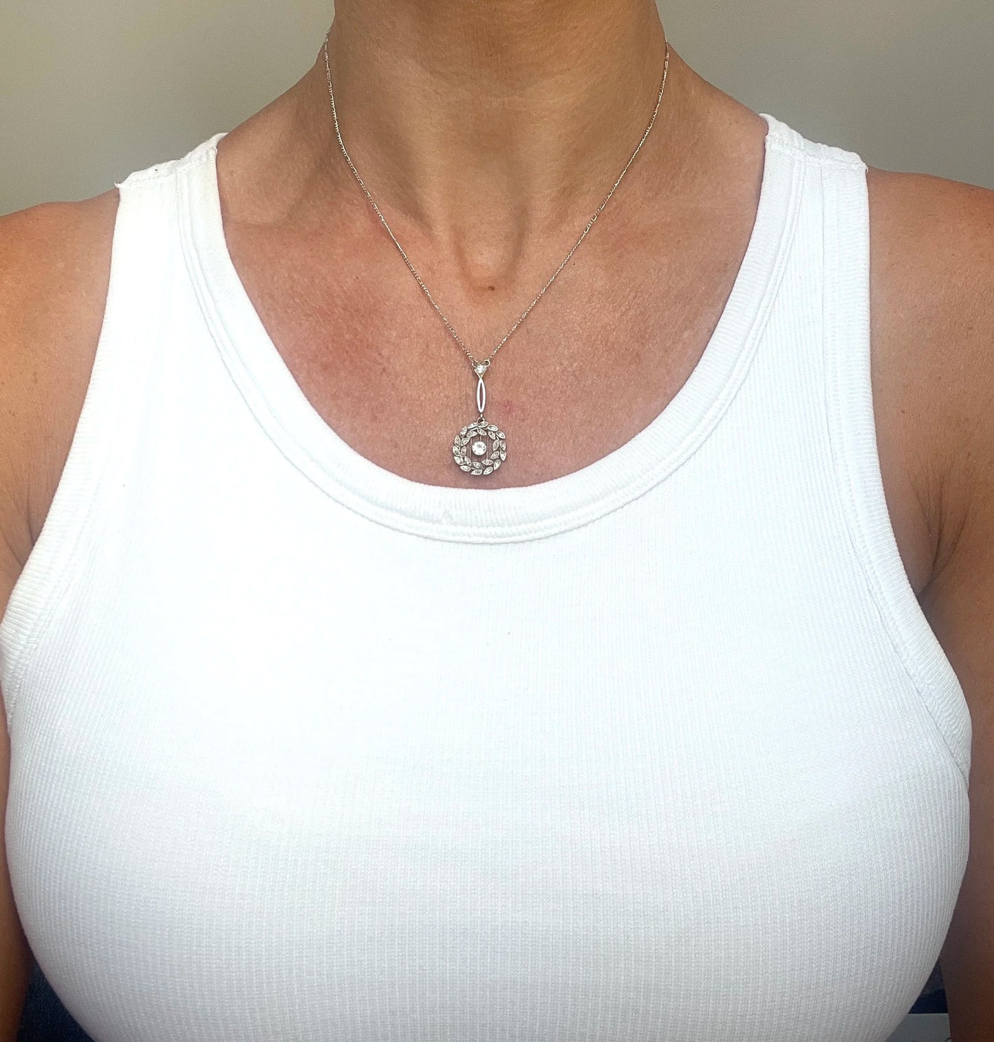 A platinum floral wreath pendant with diamonds on a platinum chain, modelled by a woman wearing a white top