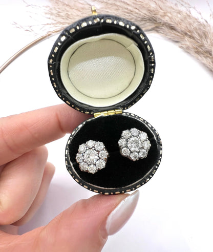 A pair of diamond daisy cluster stud earrings in yellow and white gold, in an earring box