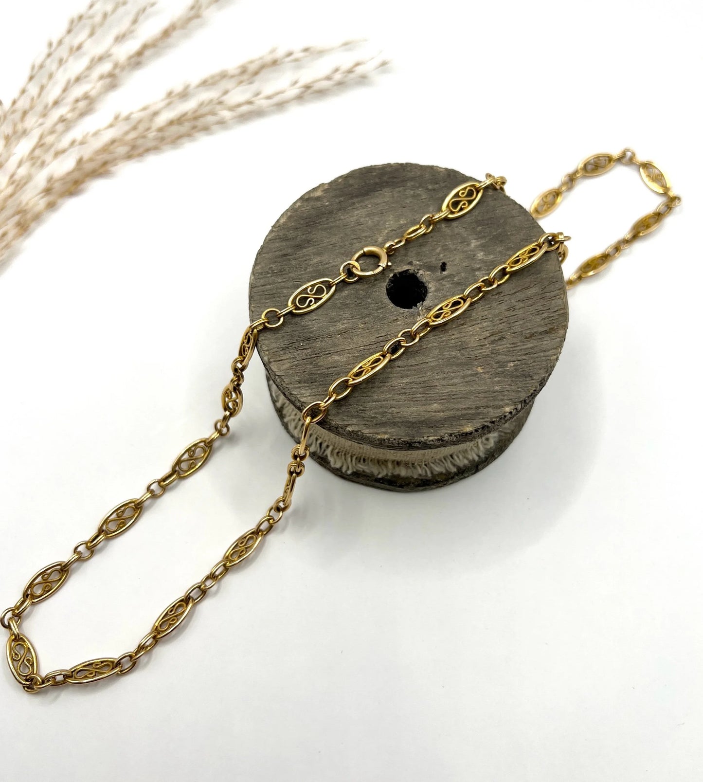 A yellow gold fancy link chain lying on a wooden object, on a white background