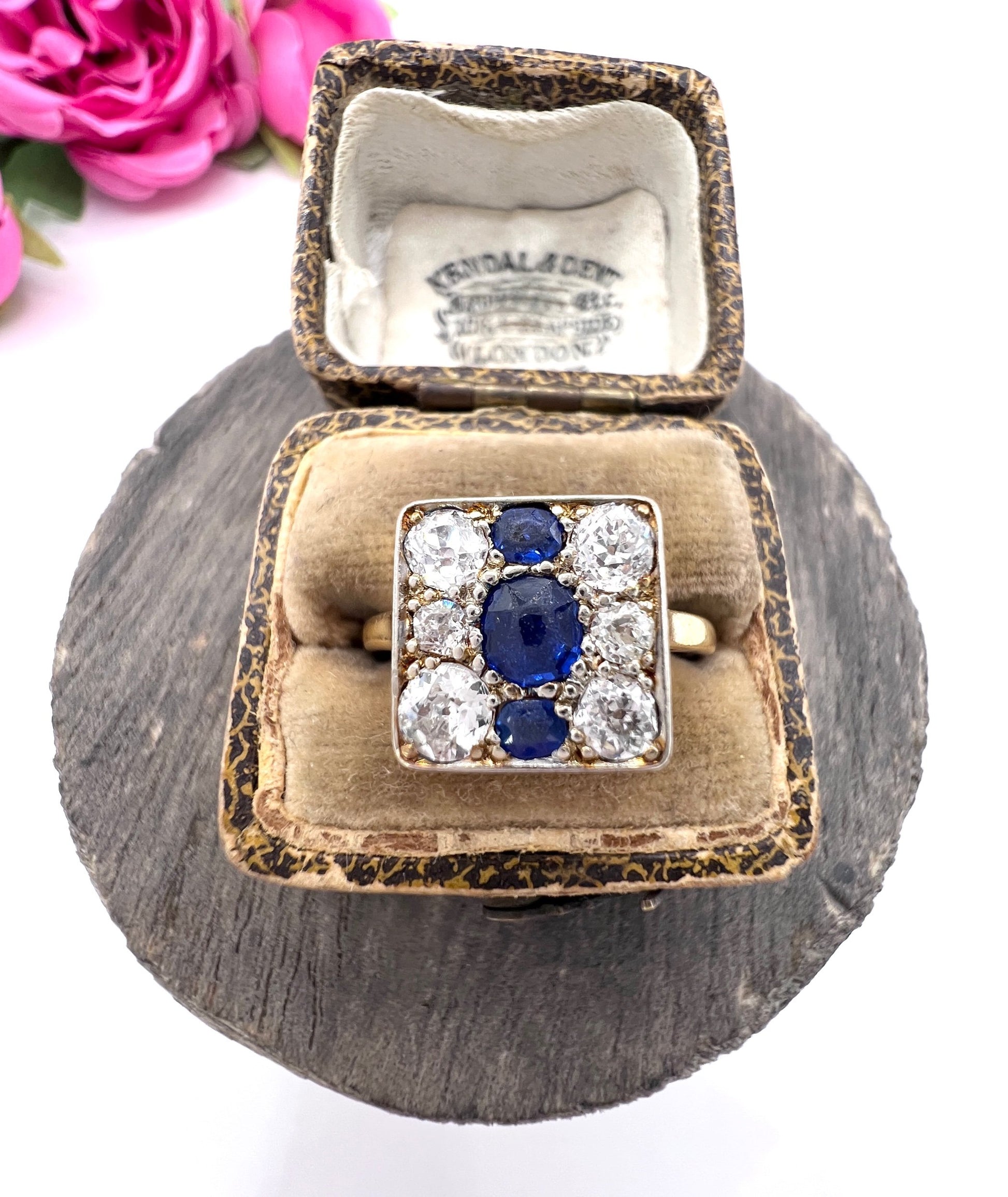 A square-shaped cluster ring with sapphires and diamonds in yellow gold and platinum, in a ring box