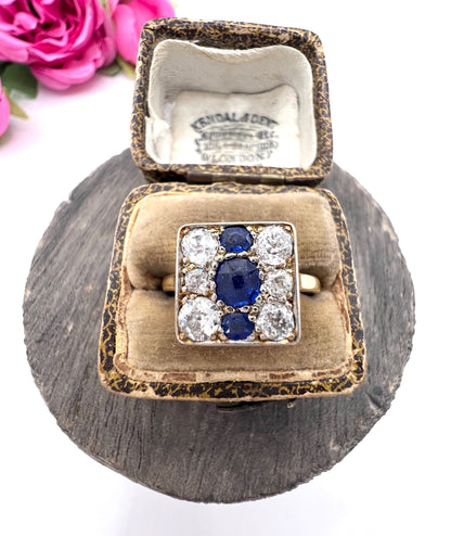 A square-shaped cluster ring with sapphires and diamonds in yellow gold and platinum, in a ring box