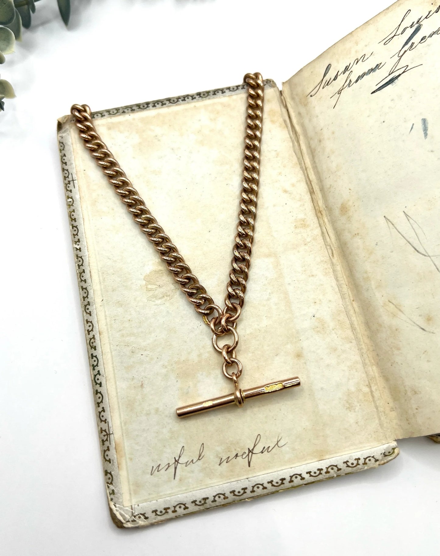 A rose gold curb link Albert chain lying on an antique book