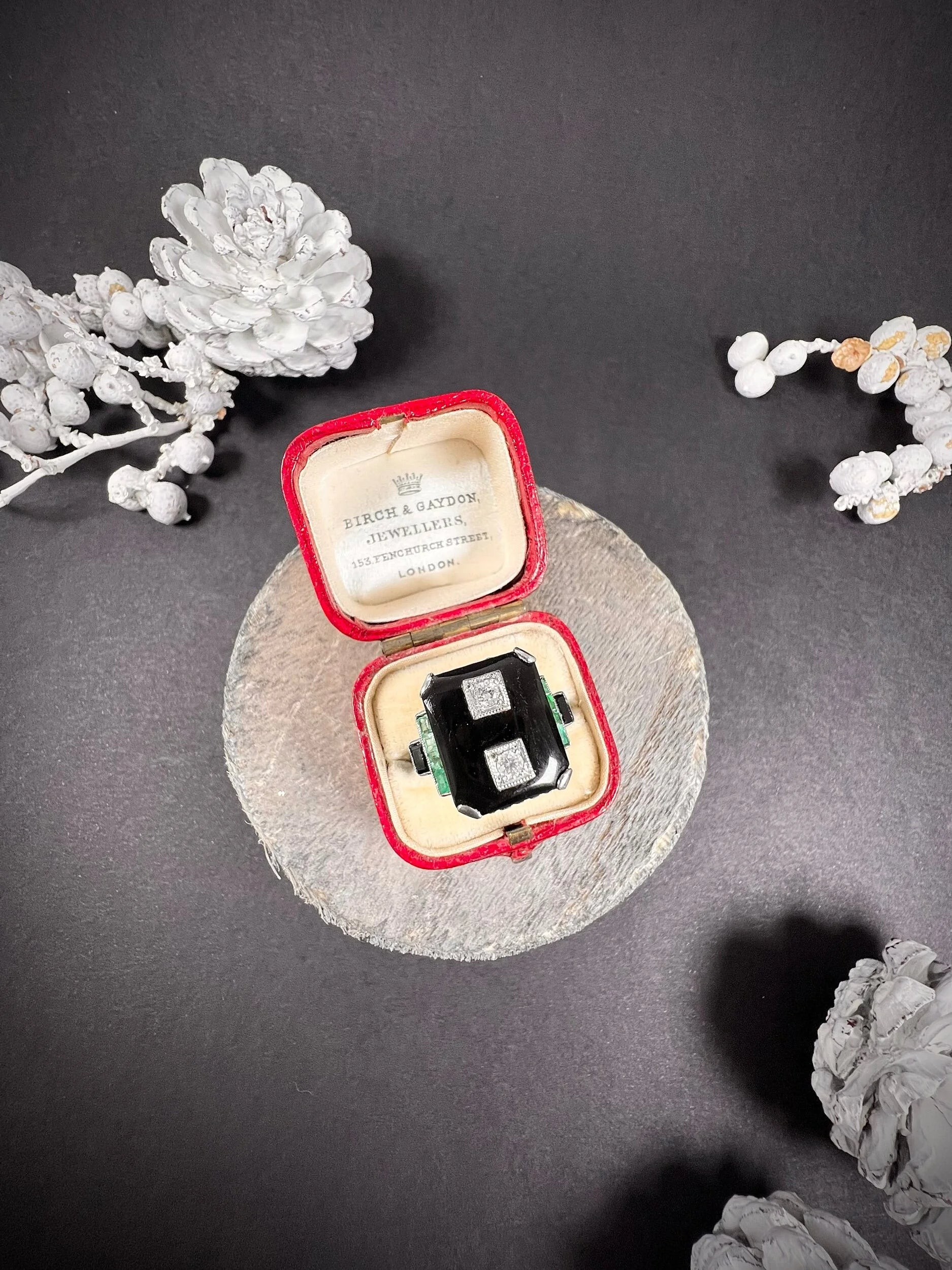 A geometric black onyx ring with diamonds and emeralds in white gold, in an antique ring box