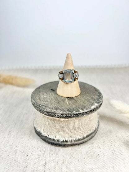 An aquamarine and diamond cocktail ring in gold, on a wooden ring cone