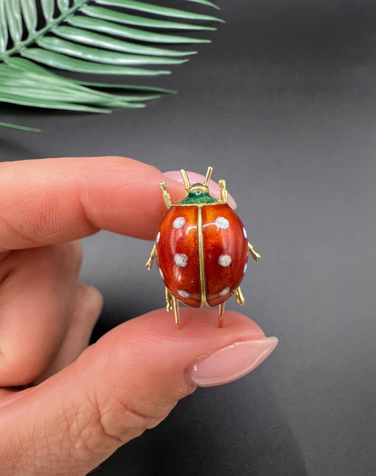 A yellow gold and enamel ladybird brooch, held in a hand