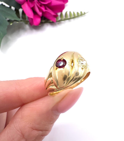 A yellow gold double headed snake ring with a ruby and a diamond, held in a hand