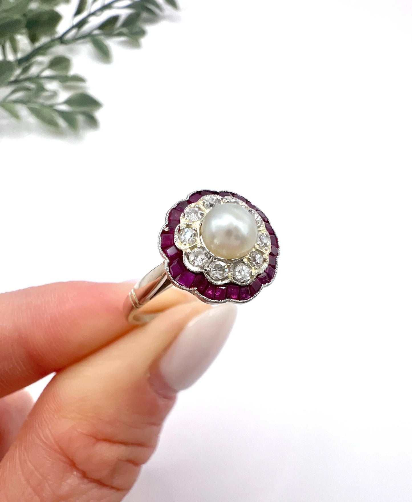 A pearl, diamond and ruby fancy cluster ring in platinum and yellow gold, held in a hand