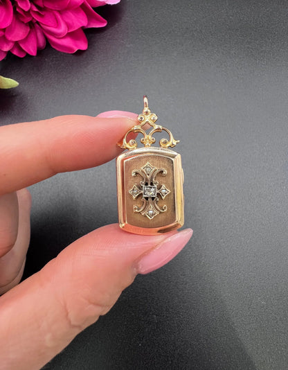 A yellow gold ornate locket with diamond fleur-de-lis detail, held in a hand