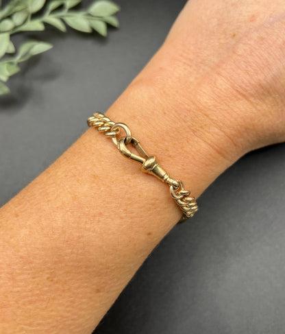 A gold curb link bracelet with a lobster claw clasp, modelled on a wrist
