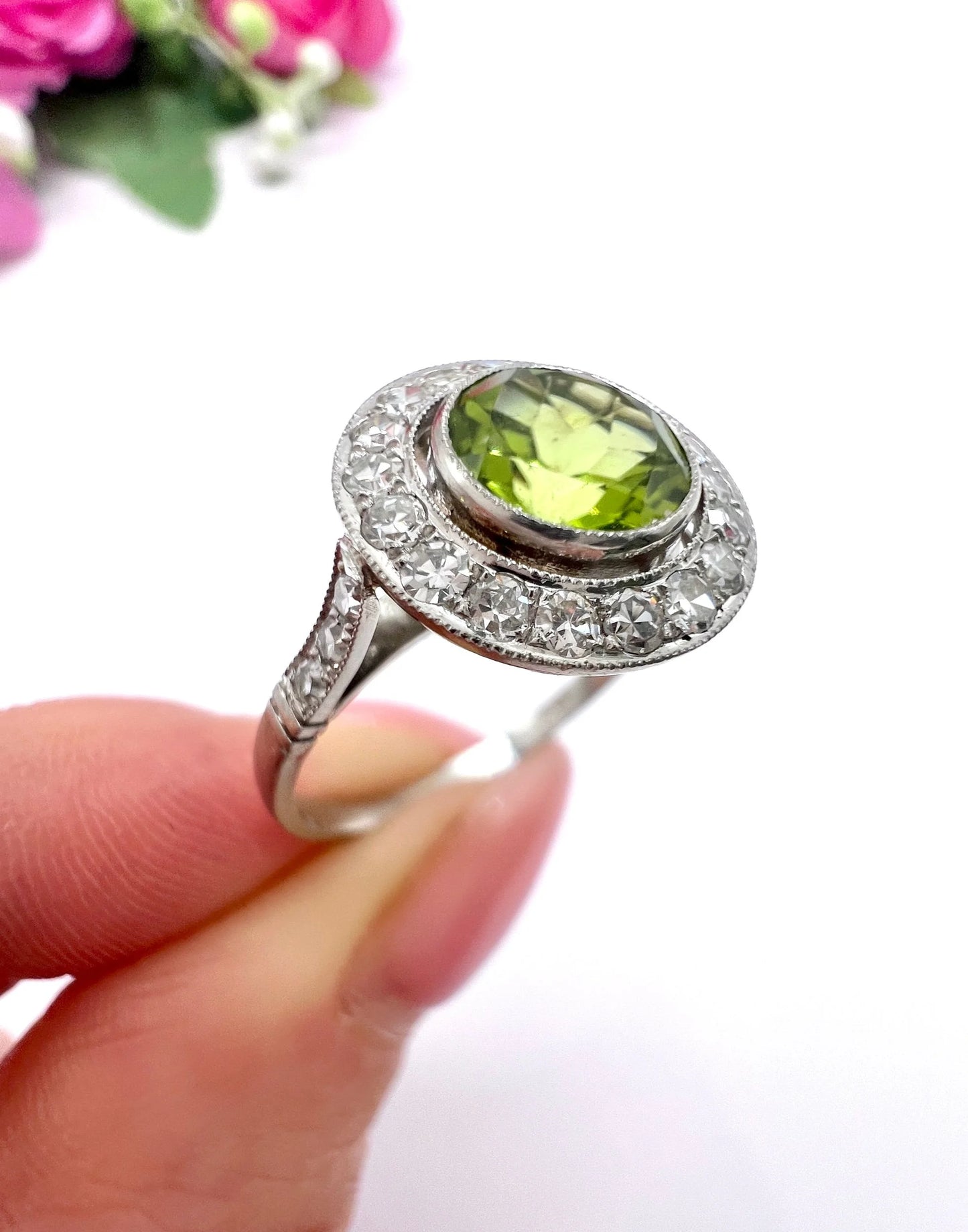 A white gold circular target cluster ring with a peridot centre surrounded by diamonds, held in a hand