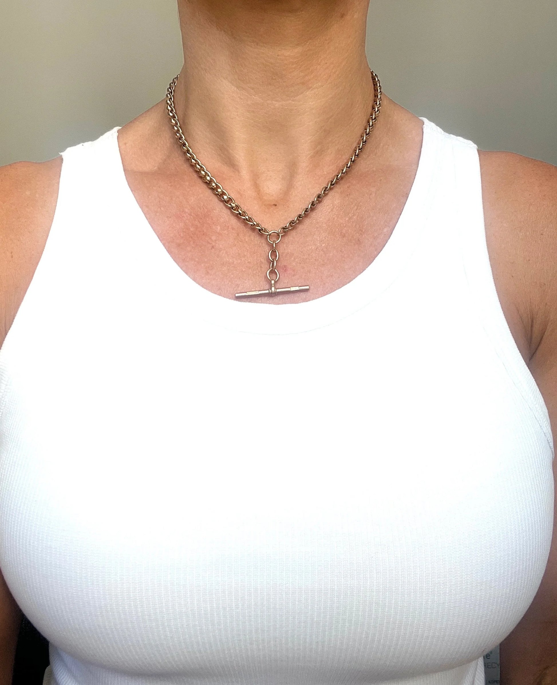 A rose gold fancy link Albert chain necklace with a T-bar attachment, modelled by a woman wearing a white top