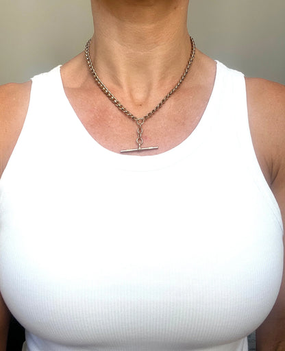 A rose gold fancy link Albert chain necklace with a T-bar attachment, modelled by a woman wearing a white top