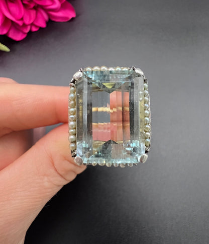 An aquamarine, pearl and diamond large cocktail ring in yellow gold and platinum, held in a hand