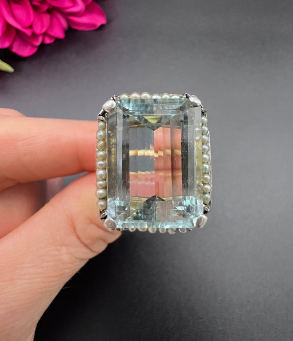 An aquamarine, pearl and diamond large cocktail ring in yellow gold and platinum, held in a hand