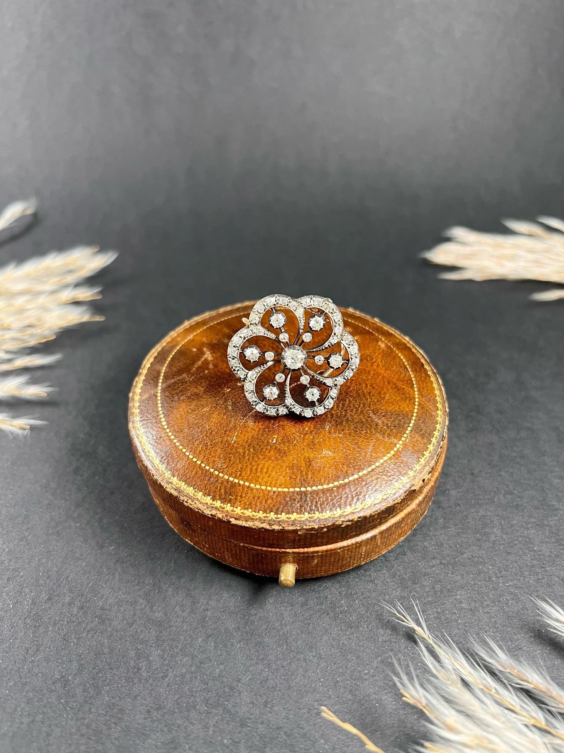 A floral design diamond set pendant/brooch on an antique brown jewellery box