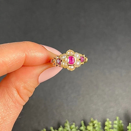 A yellow gold ruby and pearl floral cluster ring, held in a hand