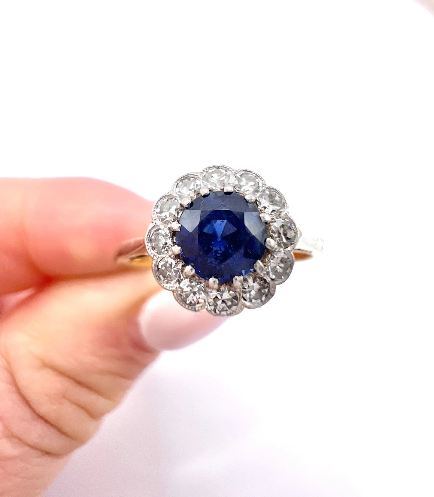A sapphire and diamond flower cluster ring in yellow gold and platinum, held in a hand