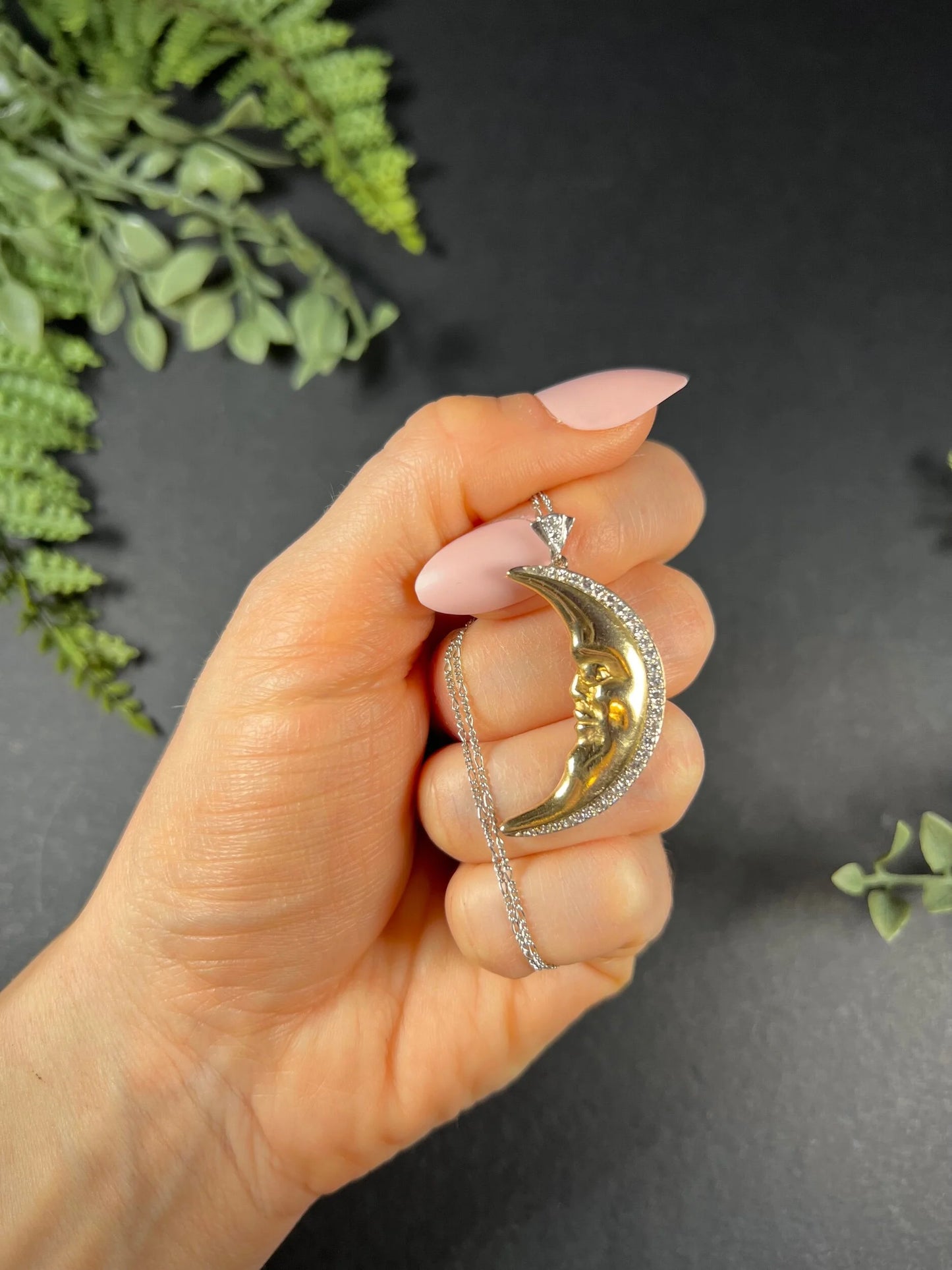 A gold crescent moon pendant with diamonds, with a chain, held in a hand