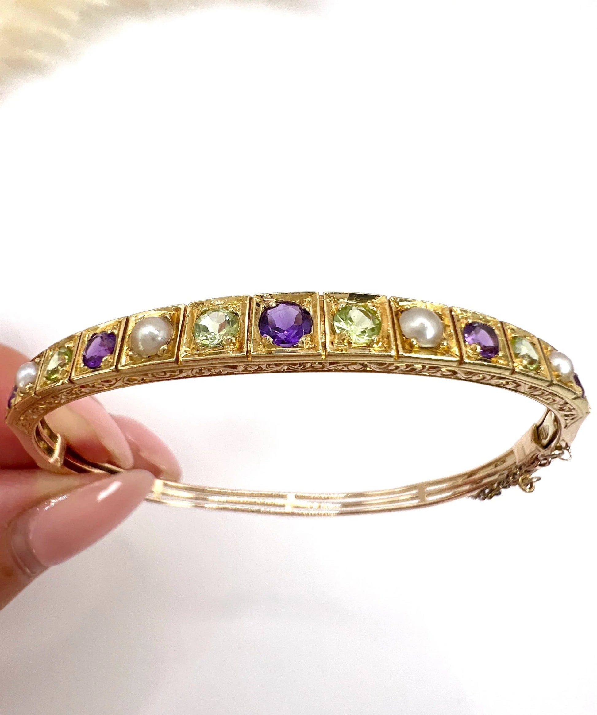 A yellow gold peridot, amethyst and pearl bangle bracelet, held in a hand