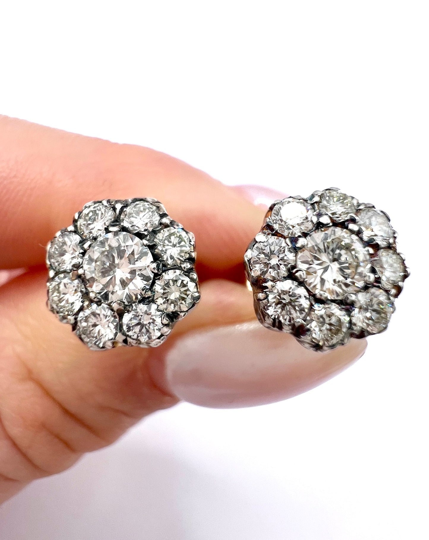 A pair of diamond daisy cluster stud earrings in yellow and white gold, held in a hand