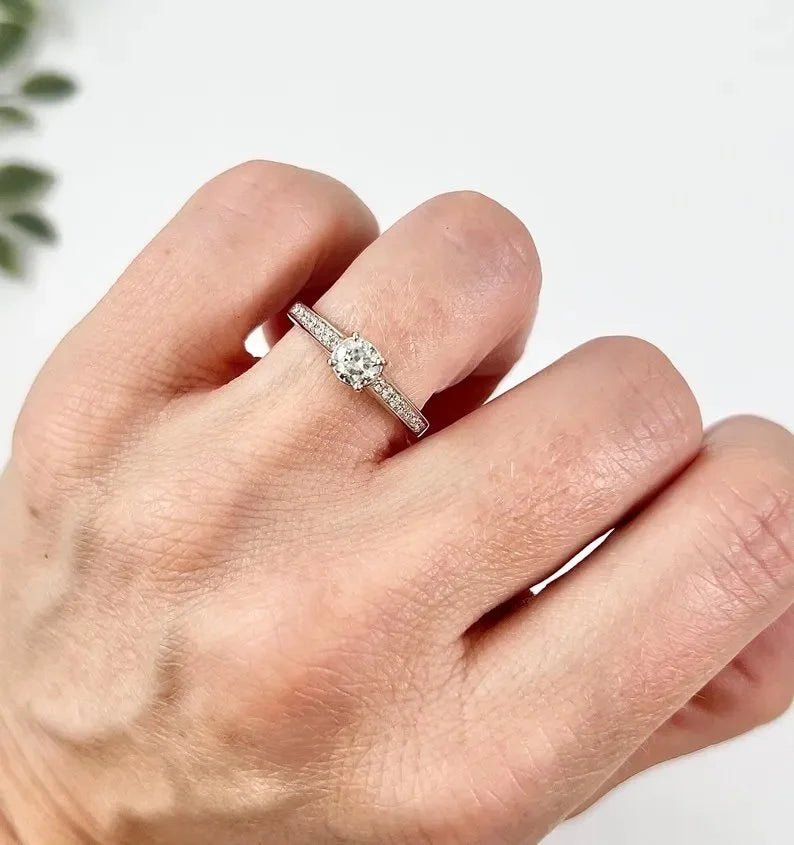 A white gold brilliant cut diamond engagement ring with diamond set shoulders, modelled on a hand