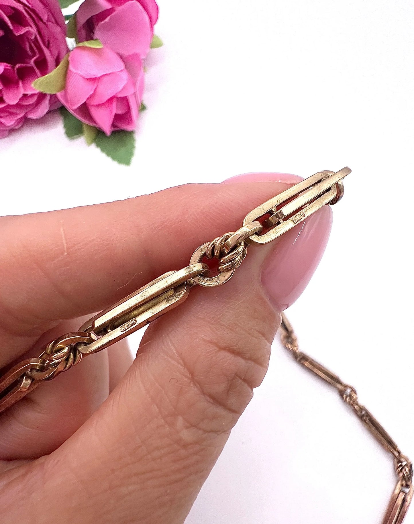 A rose gold fancy link Albert chain necklace, held in a hand