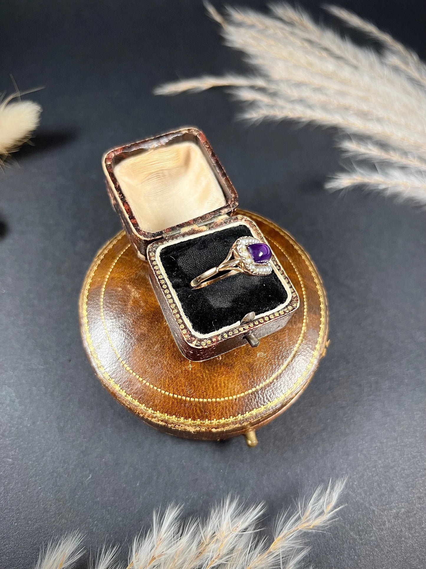 A cabochon amethyst and pearl halo cluster ring in gold, in a ring box