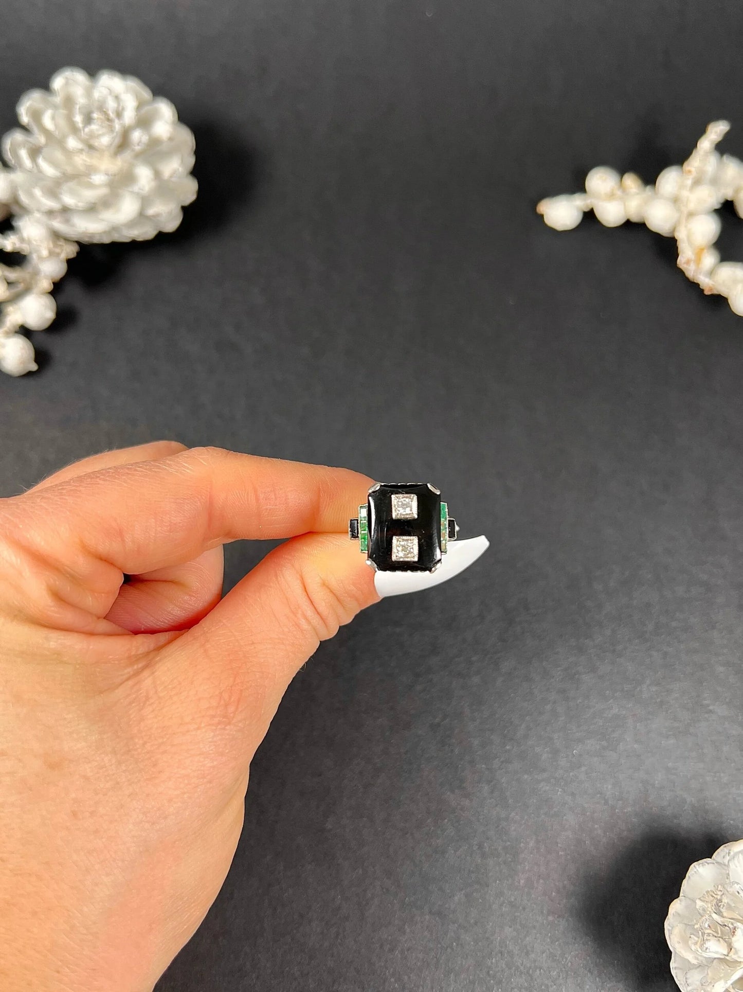 A geometric black onyx ring with diamonds and emeralds in white gold, held in a hand