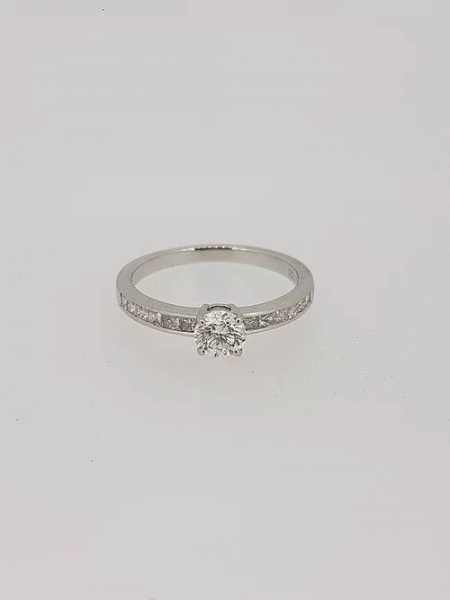 Diamond Solitaire Engagement Ring with Princess Cut Diamond Shoulders; 0.53 carat round brilliant-cut diamond, claw-set and flanked by channel-set princess-cut diamond shoulders, in 18ct white gold