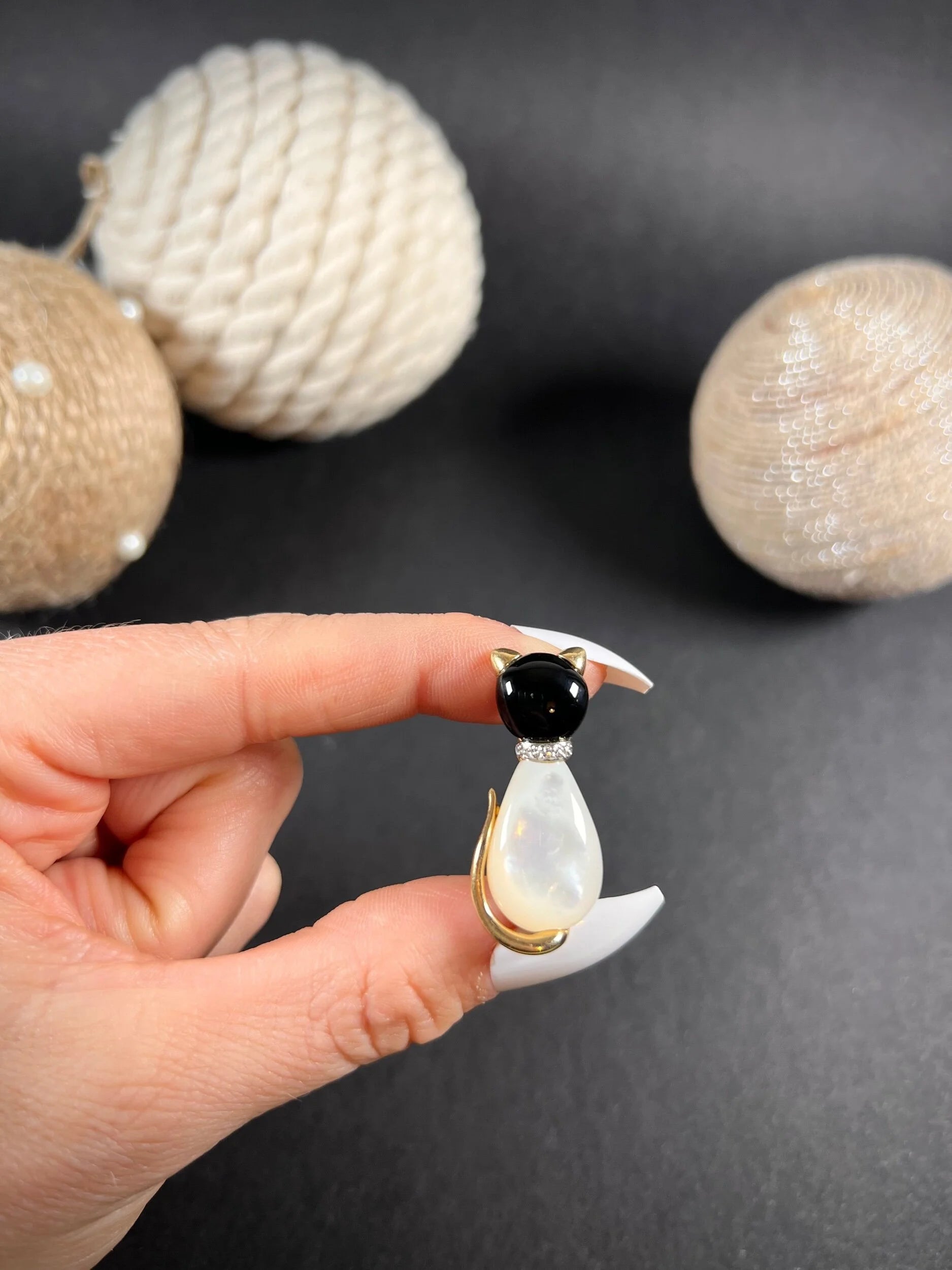 A cat-shaped brooch in yellow gold with black onyx, mother of pearl and a diamond set collar, held in a hand