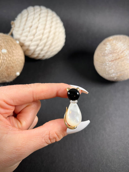 A cat-shaped brooch in yellow gold with black onyx, mother of pearl and a diamond set collar, held in a hand