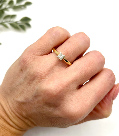 A solitaire princess cut diamond ring in yellow and white gold, modelled on a hand