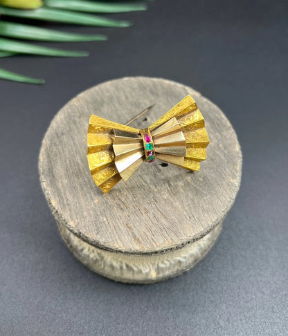 A yellow gold bow shaped brooch with rubies and emeralds