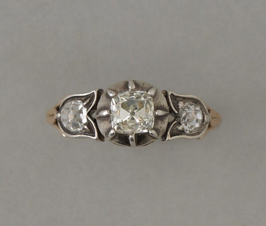 Antique Victorian Old Cut Diamond Three Stone Ring; central 0.80ct old cushion cut diamond set in a cut away silver bezel, flanked on each side by little silver tulip set with an old cut diamond, on 18ct rosé gold shank .France, 19th century