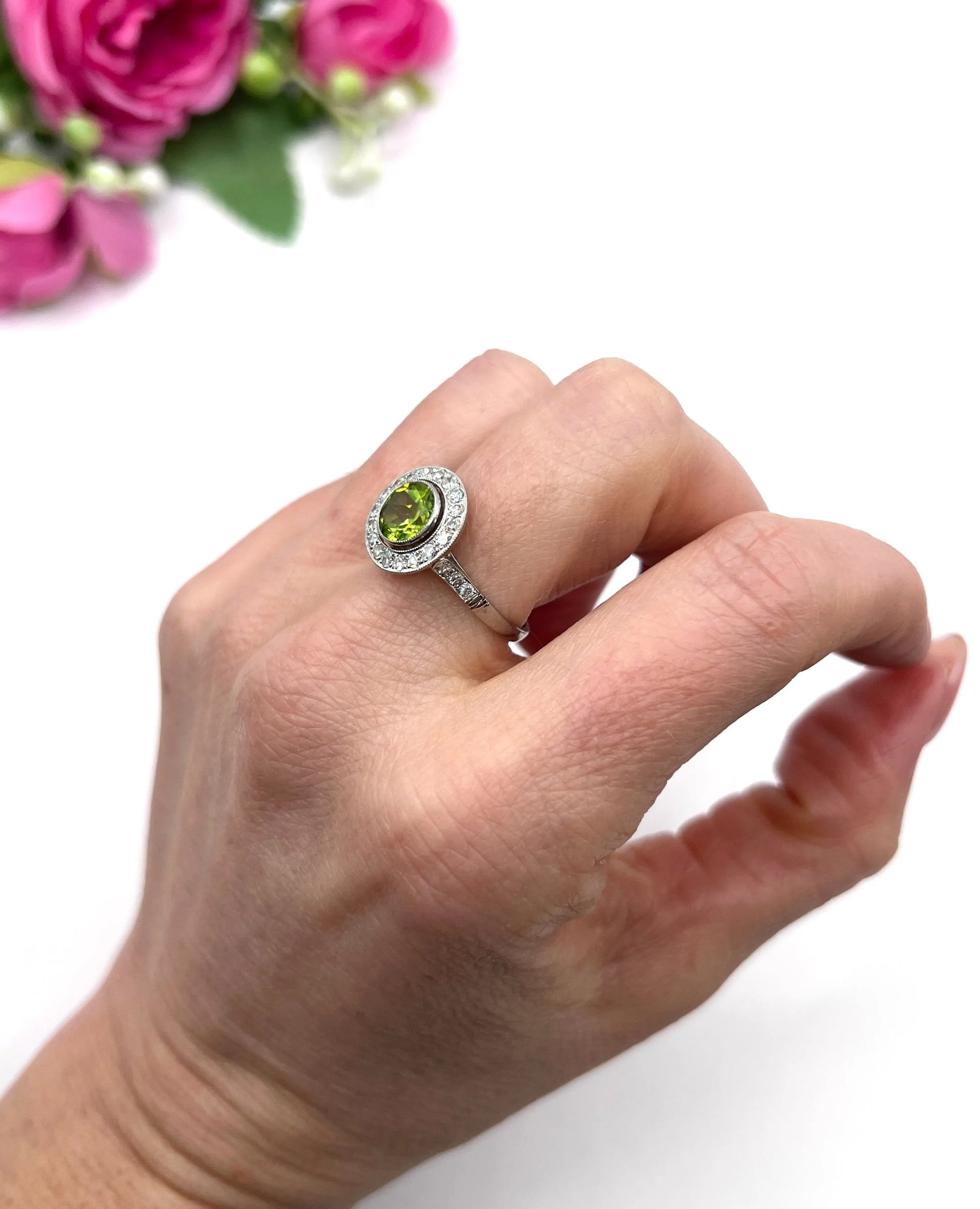 A white gold circular target cluster ring with a peridot centre surrounded by diamonds, modelled on a hand