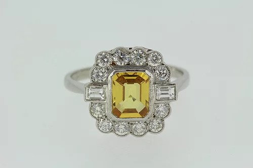 Yellow Sapphire and Diamond Floral Cluster Ring; 1.75 carat emerald-cut yellow sapphire within a 0.85ct brilliant and baguette-cut diamond surround, in 18ct white gold